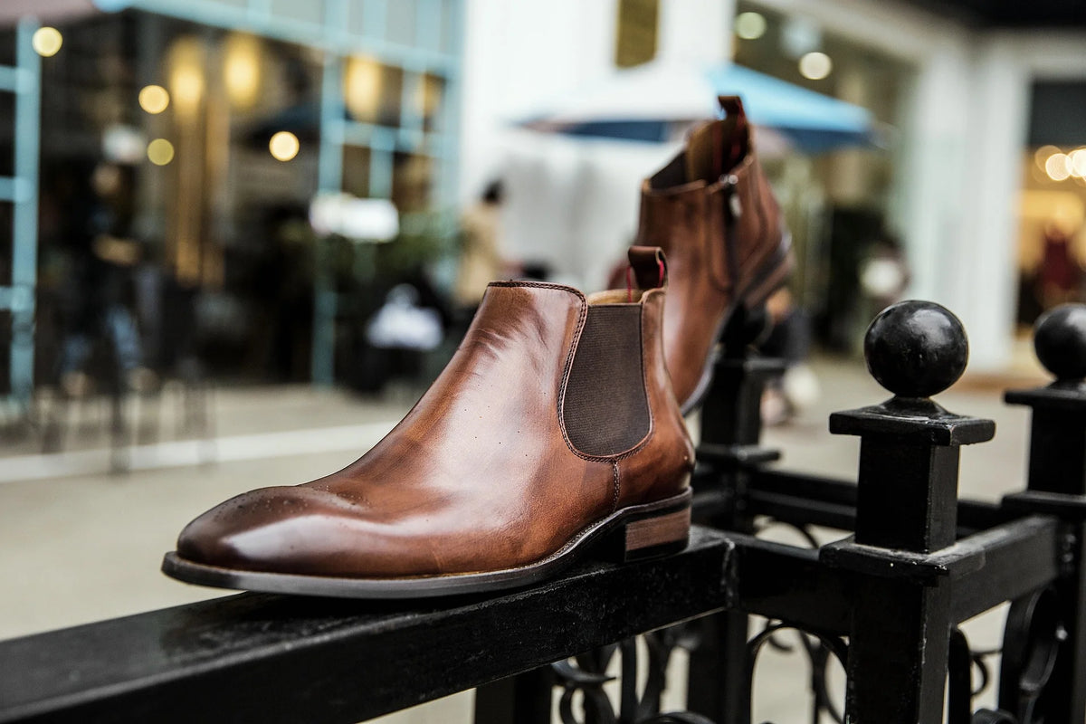Brown Chelsea boot resting on a black iron railing